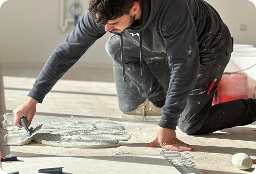 artisan carreleur chapiste, Ouvrier posant des carreaux au sol, appliquant du mortier-colle avec une truelle à Saint-Nazaire-de-Pezan près de Montpellier dans l'Hérault 34