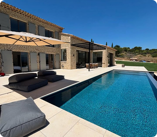 Luxueuse villa en pierre avec piscine, terrasse, parasol et paysage verdoyant sous ciel bleu à Saint-Nazaire-de-Pezan près de Montpellier dans l'Hérault 34