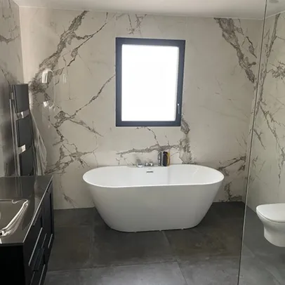 Salle de bain moderne avec baignoire autoportante, mur en marbre, fenêtre et meuble-lavabo sombre à Saint-Nazaire-de-Pezan près de Montpellier dans l'Hérault 34