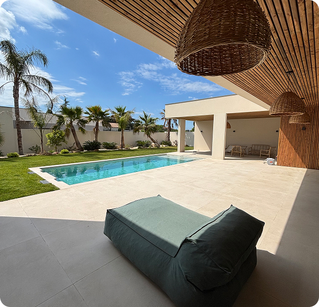 Une piscine extérieure lumineuse avec des palmiers et une terrasse couverte, un pouf vert à Saint Nazaire de Pézan près de Montpellier dans l'Hérault 34