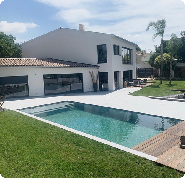 Piscine moderne rectangulaire et terrasse ensoleillée devant une grande maison blanche à Saint Nazaire de Pézan près de Montpellier dans l'Hérault 34